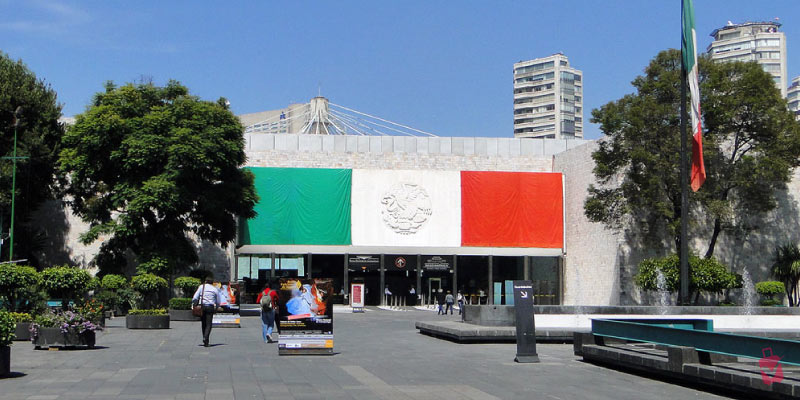 Museo Nacional de Antropología, Mexico's vibrant flag drapes the entrance of a modern museum building.