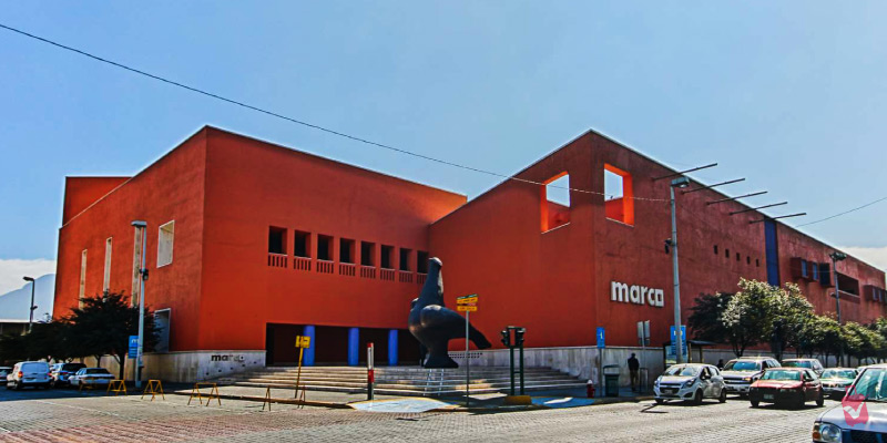The Museum of Contemporary Art of Monterrey, a red building with a large sculpture in front, and cars parked on the street.