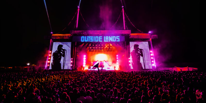 Concert goers enjoy a nighttime performance at the Outside Lands Music and Arts Festival with vibrant stage lighting.