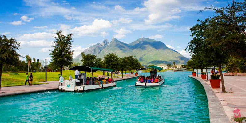 Boats with people cruising along the turquoise waters of Paseo de Santa Lucía, with lush greenery and mountains in the background.