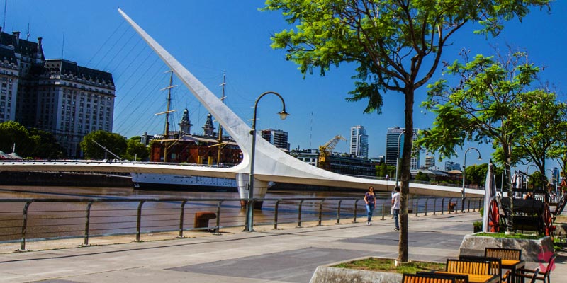The Puente de las Damas, a modern pedestrian bridge with a unique design, stretching across a river in a sunny city scene, possibly in Guadalajara.