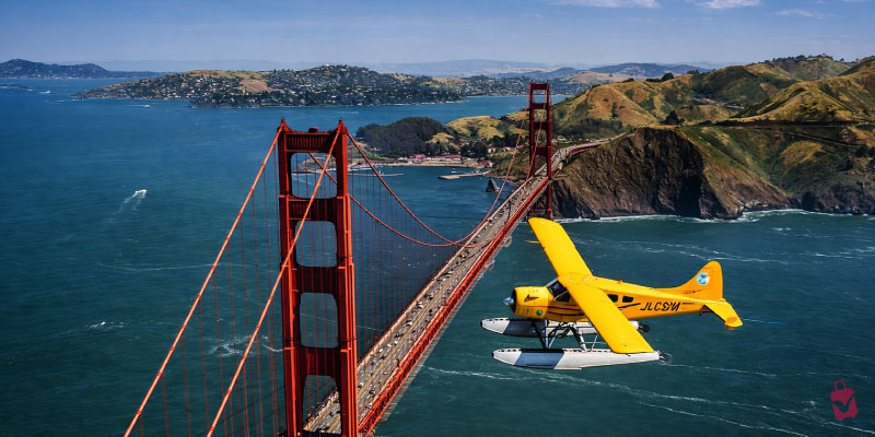 A bright yellow plane flies near the Golden Gate Bridge during scenic seaplane tours offering aerial views of the bay.