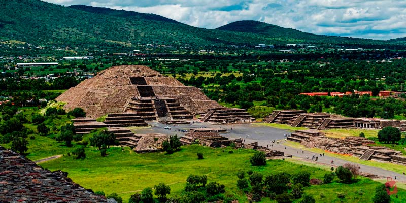 Teotihuacán pyramids amid lush greenery under a cloudy sky, an ancient Mexican marvel.