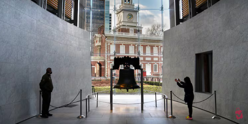 Visitors view the Liberty Bell inside its glass pavilion with the historic Independence Hall visible in the background.