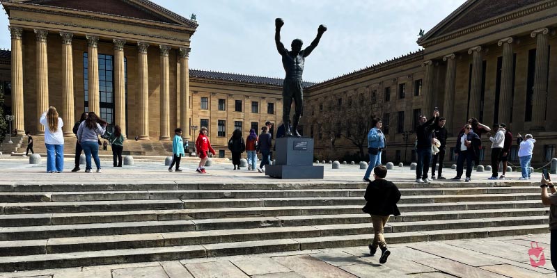 Tourists gather at the bronze statue of a boxer located at the bottom of the Rocky Steps leading to the art museum.