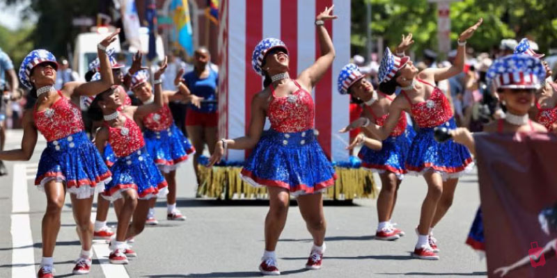 Performers in sparkling red, white, and blue outfits with star-spangled hats dance in a parade during The Semiquincentennial Celebration.