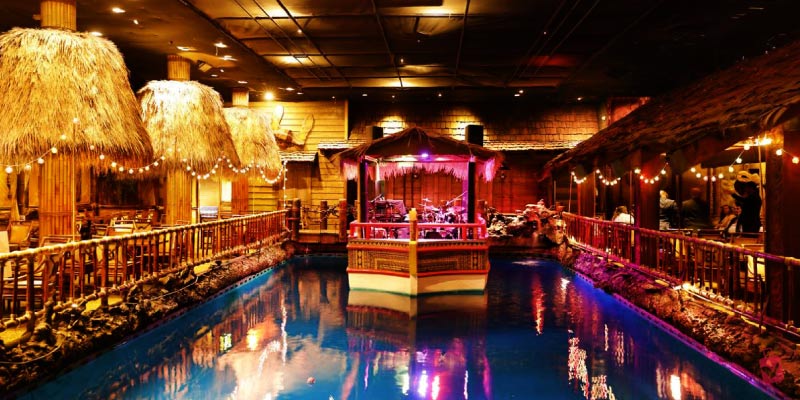 The tropical interior of The Tonga Room and Hurricane Bar features a central pool, thatched huts, and island-themed decor.