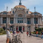A sunny day at the Palacio de Bellas Artes, with people walking and biking around the grand architectural landmark, showcasing things to do in Mexico City.