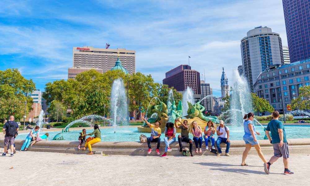 People relax by Swann Memorial Fountain at Logan Circle, highlighting popular things to do in Philadelphia like visiting scenic urban parks.