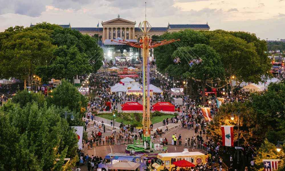 An aerial view of a bustling fairground with rides and crowds during one of Philadelphia's upcoming festivals.