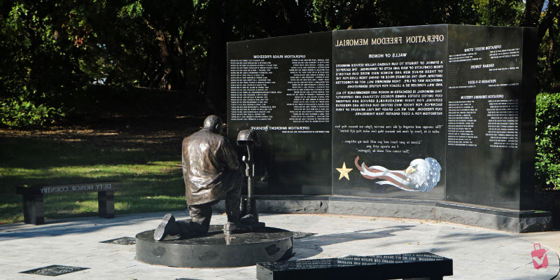 The Vietnam Veterans Memorial features a kneeling soldier statue in front of a black wall with etched names and an American flag design.