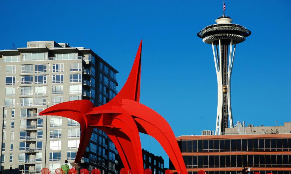 The vibrant red "Eagle" sculpture by Alexander Calder in Seattle, with the Space Needle and other buildings under a clear blue sky.