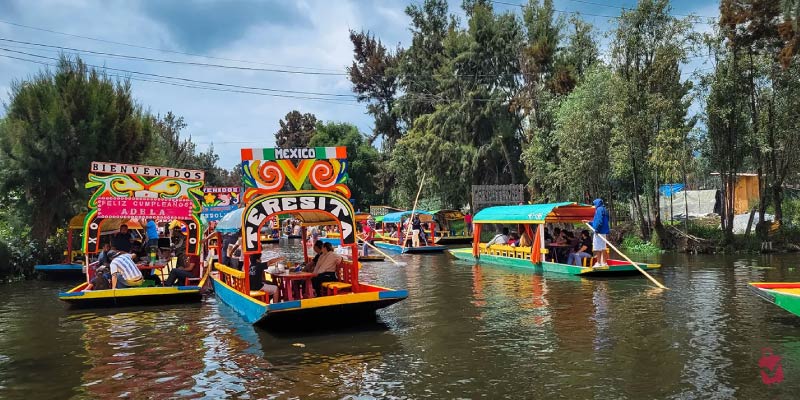 Xochimilco's colorful trajineras, vibrant boats, glide through canals filled with people enjoying a festive day in Mexico.