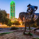 A cowboy statue overlooks the neon green skyline showing one of the historical landmarks in Dallas