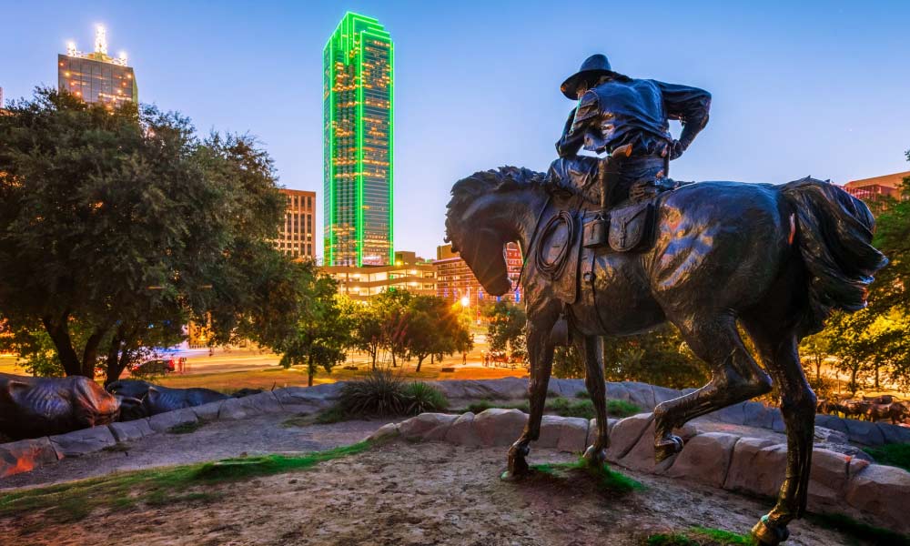 A cowboy statue overlooks the neon green skyline showing one of the historical landmarks in Dallas