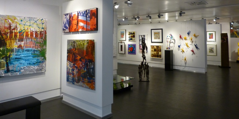 The interior of Harbour View Gallery showcases vibrant contemporary paintings and unique wall sculptures in a modern, well-lit space.