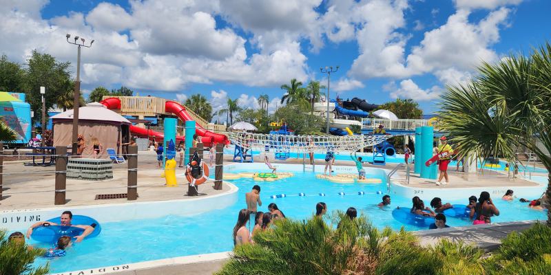 Families cool off in the bright blue pools and lazy river at Sun Splash Family Waterpark, featuring colorful water slides in the background.